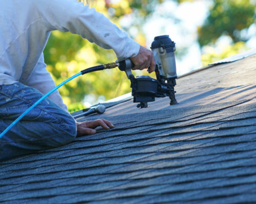 Handyman Using Nail Gun To Install Shingle To Repair Roof